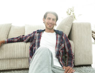 Kendine güvenen adam rahat bir oturma odasında halı üzerinde oturan.