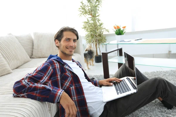 Encantador jovem com laptop sentado na sala de estar moderna — Fotografia de Stock