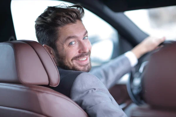 Вид сзади, молодой человек за рулем автомобиля, смотрит в камеру — стоковое фото
