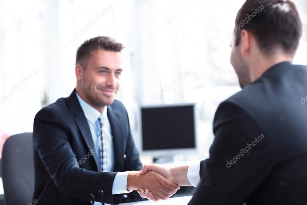 handshake of business partners sitting at a Desk