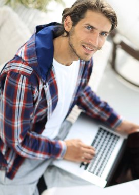 dizüstü bilgisayarda çalışan ve kameraya bakarak bir genç adam. Yukarıdan görüntülemek