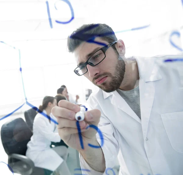 from behind the glass.scientist writes a marker on a glass Board.