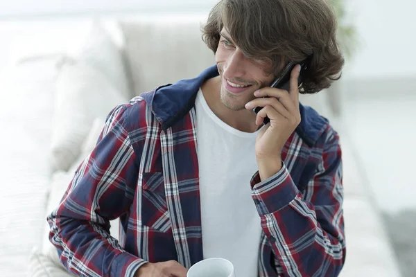 Hermoso chico con una taza se sienta delante de un ordenador portátil . — Foto de Stock