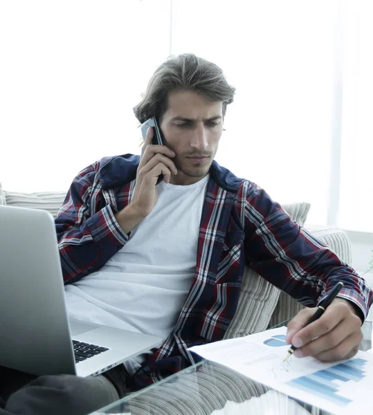 Young man working with financial documents sitting on sofa in living room — Stock Photo, Image