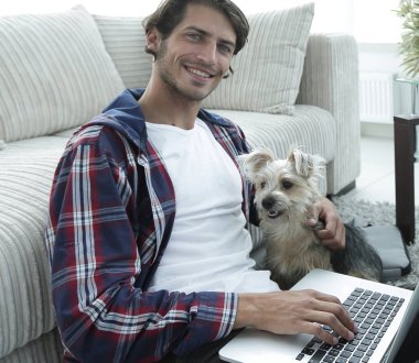 yakışıklı adam köpeğini sarılma ve kanepede oturan dizüstü bilgisayar ile