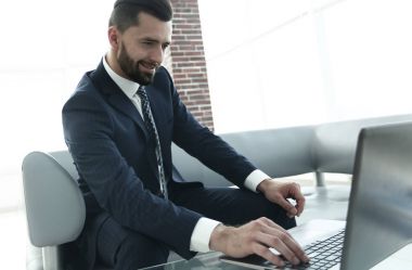 ofis lobisinde otururken dizüstü bilgisayar üzerinde çalışan iş adamı