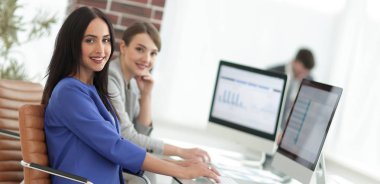 Kameraya bakarak ve oturma işyerinde gülümseyen genç kadın