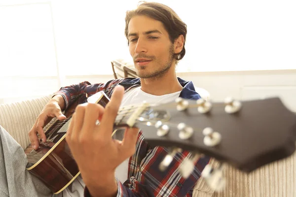 Um tipo com uma guitarra sentada no sofá na sala de estar. conceito de um estilo de vida — Fotografia de Stock