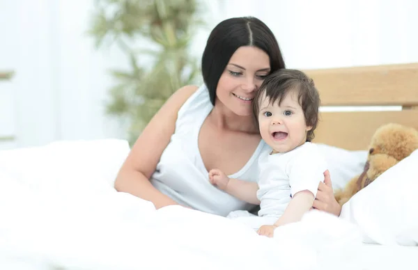 Yatakta yatan ve gülümseyen bir bebek ile güzel genç anne — Stok fotoğraf
