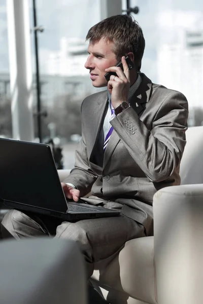 Atractivo tipo europeo hablando por teléfono mientras usa el ordenador portátil . — Foto de Stock