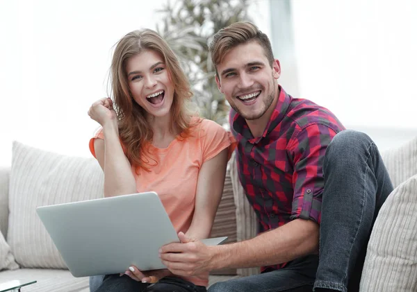 Jovem casal se alegra, sentado no sofá em frente ao laptop aberto — Fotografia de Stock