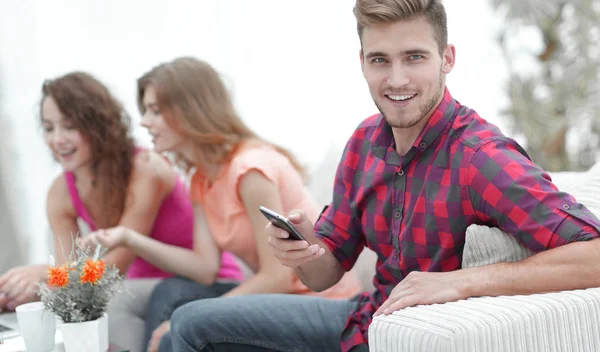 Tipo moderno con un teléfono inteligente y sus amigos sentados en el sofá — Foto de Stock