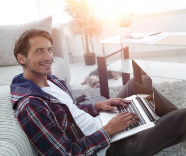 gülümseyen adam kanepede yakın katta oturan bir dizüstü bilgisayar ile