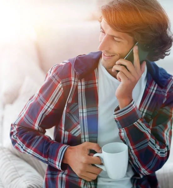 Hermoso chico con una taza se sienta delante de un ordenador portátil . — Foto de Stock