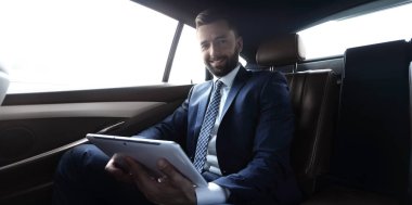 bir arabanın arka koltuğunda çalışma ve bir tablet kullanarak iş adamı