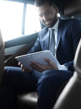 bir arabanın arka koltuğunda oturan bir dijital tablet ile işadamı