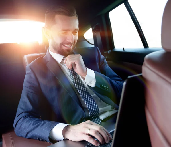Empresário lê informações sobre laptop enquanto sentado no carro — Fotografia de Stock