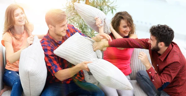 Gruppo di amici che giocano a pillow fight, seduti sul divano — Foto Stock