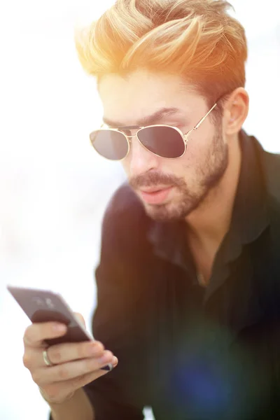 En snygg skäggiga män sitter och använder en smartphone. — Stockfoto