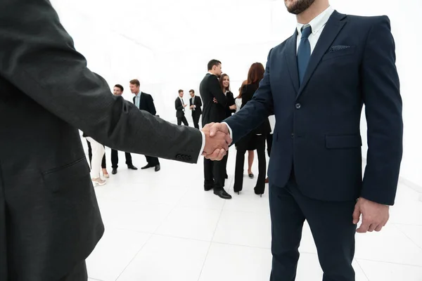Крупный план рукопожатия деловых партнеров на фоне деловой команды — стоковое фото