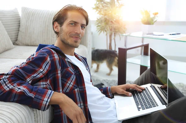 Okouzlující mladý muž s notebookem sedět v moderním obývacím pokoji — Stock fotografie