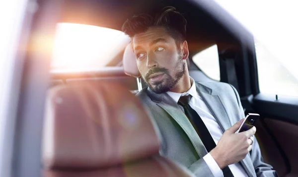 Hombre de negocios no sonriente sentado en el asiento trasero en su coche — Foto de Stock