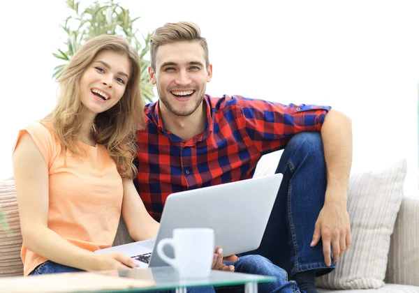 Young couple of students uses a laptop sitting on sofa — Stock Photo, Image