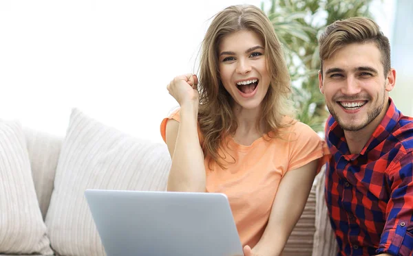 Young couple rejoices,sitting on the couch in front of the open laptop — Stock Photo, Image