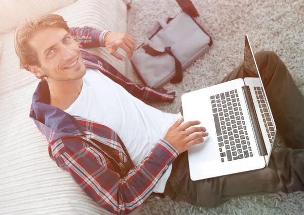 Zakelijke man met laptop zitting op tapijt in de woonkamer. — Stockfoto