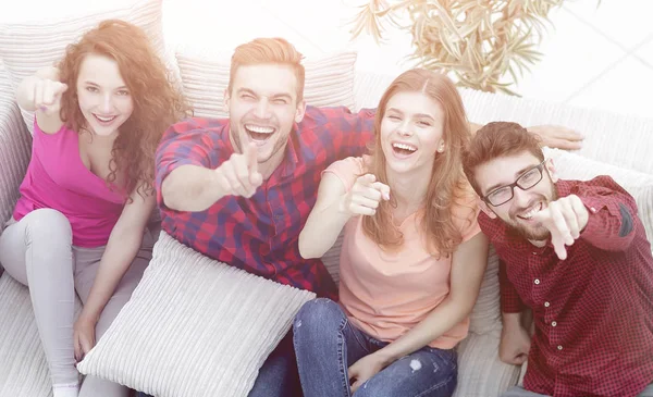 group of laughing friends sitting on sofa and showing forefinger
