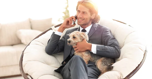 businessman holds his pet and talks on the smartphone while sitt