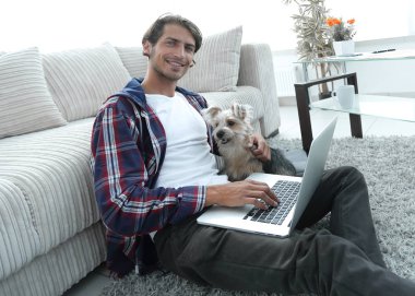 yakışıklı adam köpeğini sarılma ve kanepede oturan dizüstü bilgisayar ile