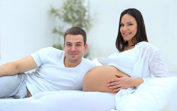 Смеющаяся белая беременная женщина лежит в постели со своим мужем в спальне — стоковое фото