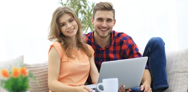 Pareja joven .working en el ordenador portátil sentado en el sofá —  Fotos de Stock