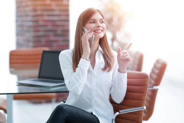 Ofiste oturan iş kadını cep telefonuyla konuşuyor.