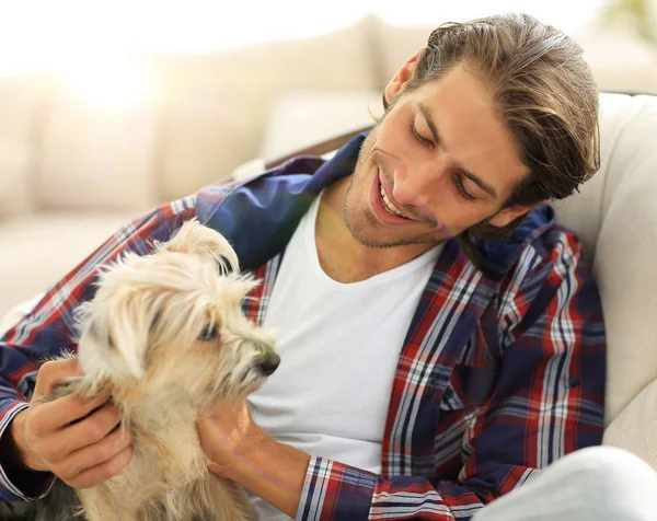 Stilig kille strök hans hund när man sitter i en stor fåtölj. — Stockfoto