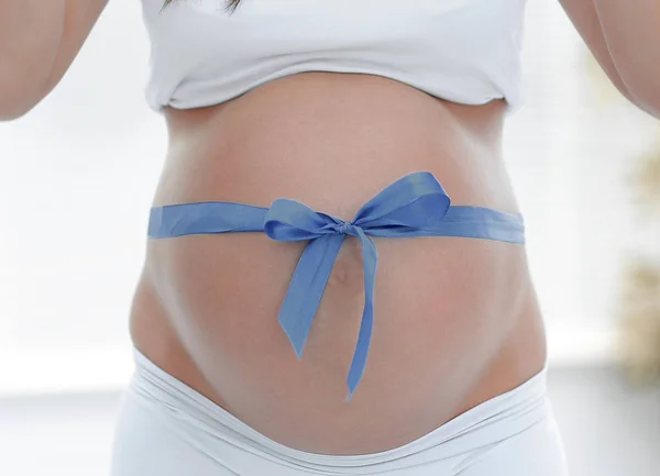 Close up van een lachende zwangere vrouw koppelverkoop een blauw lint op haar buik. — Stockfoto