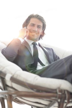 iş adamı rahat bir sandalyede otururken Smartphone'da konuşuyor.