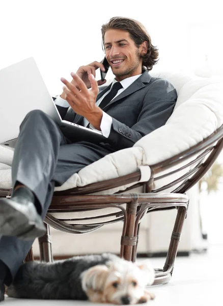 Onun evinde sandalyede oturan smartphone cep telefonu ile konuşurken işadamı — Stok fotoğraf