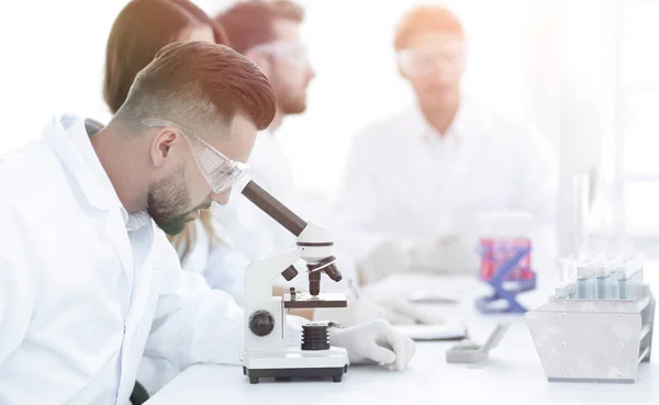 Científico mirando en un microscopio sentado en el laboratorio . — Foto de Stock