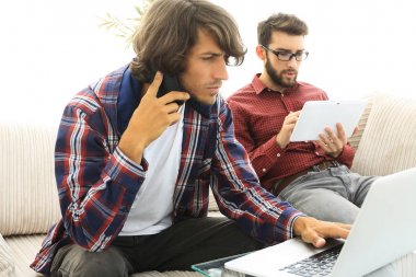 kanepede oturan, bir cep telefonu üzerinde konuşurken ve internette chat yapan iki adam.