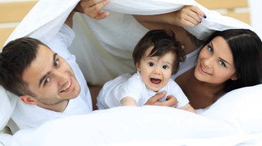 mutlu bir aile kameraya bakarken bir yorgan altında poz