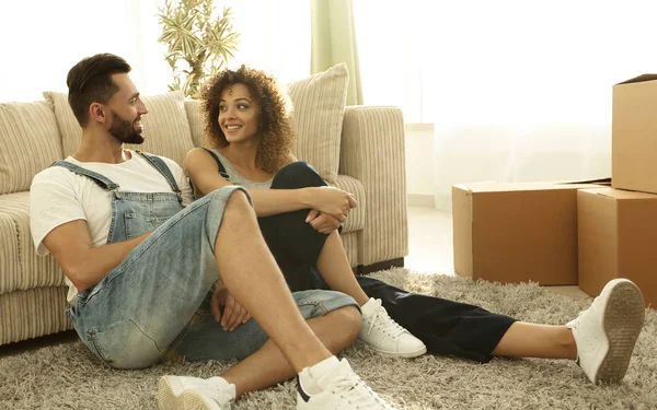Feliz pareja de casados sentados en la alfombra en un nuevo apartamento . — Foto de Stock