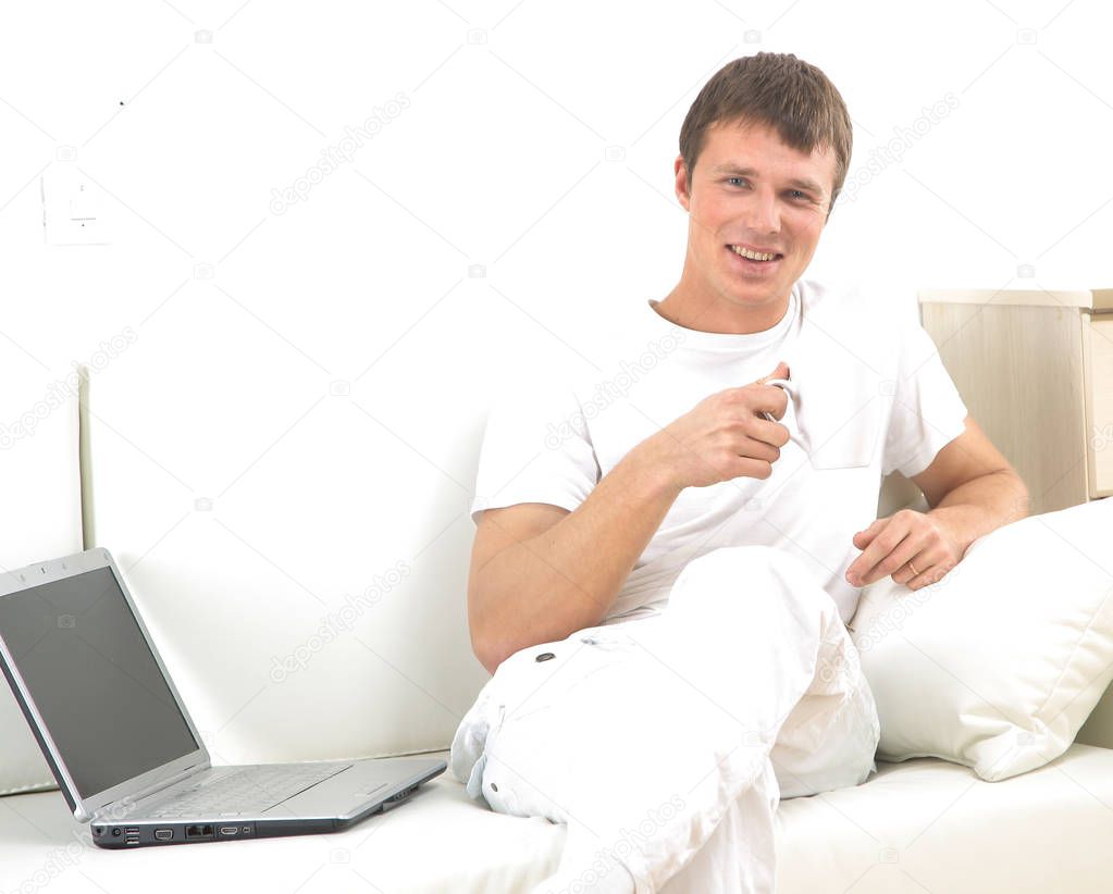 Handsome casual man sitting on couch having coffee at home.
