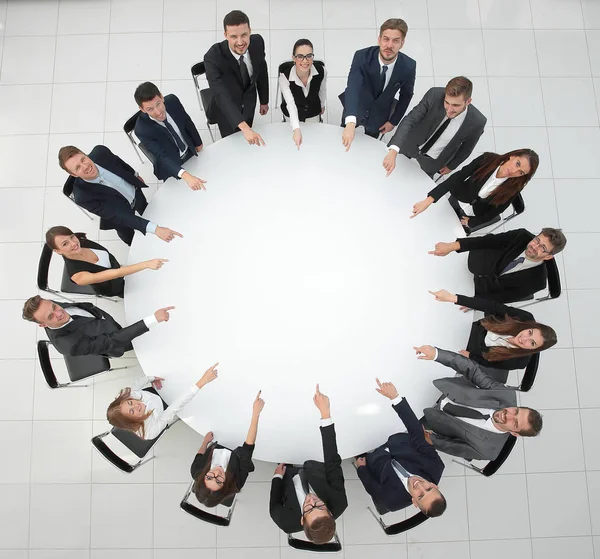 Zespół biznesowy wskazuje centrum okrągłego stołu. — Zdjęcie stockowe