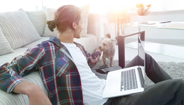 Stijlvolle jongeman streelde zijn huisdier en bezig met laptop — Stockfoto