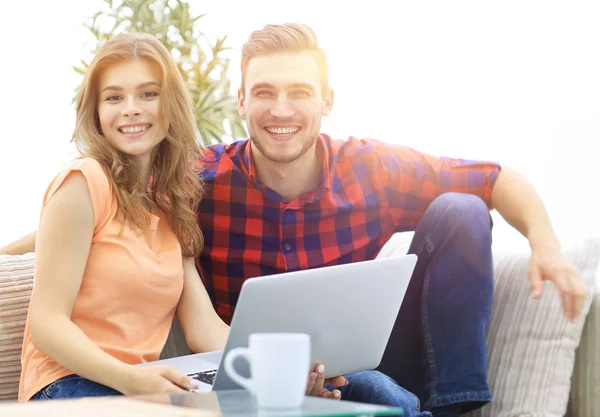 Young couple of students uses a laptop sitting on sofa — Stock Photo, Image