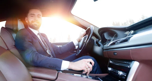 View from the side confident businessman sits at the wheel of a — Stock Photo, Image