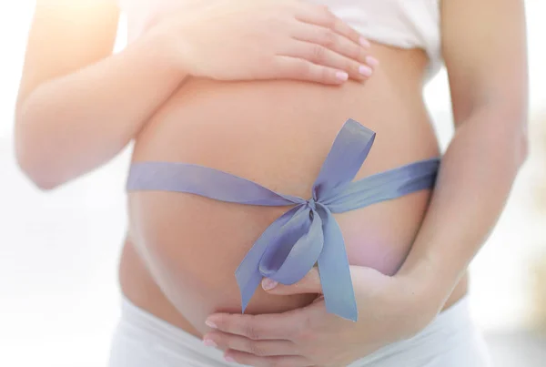 Close-up de uma mulher grávida amarrando uma fita azul em sua barriga — Fotografia de Stock