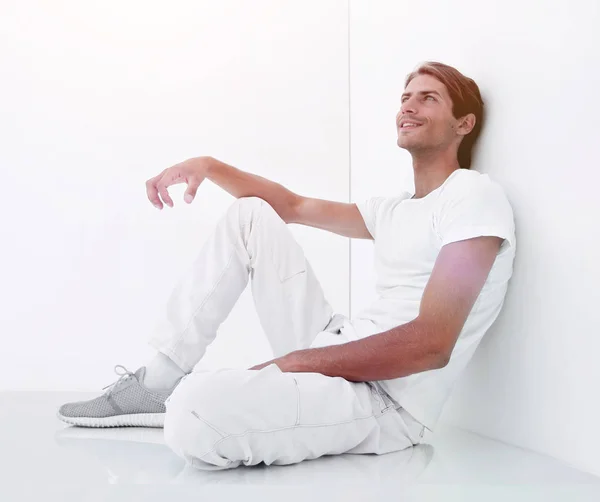 Ονειρική νεαρός άνδρας κάθεται δίπλα σε ένα λευκό τοίχο. — Φωτογραφία Αρχείου